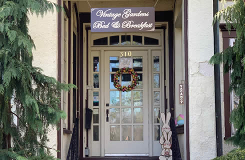 Entryway with a wood and glass door with a sign overhead: Vintage Gardens Bed & Breakfast