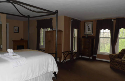:arge bedroom with black iron canopy bed, a floral sofa, and four windows with dark draperies.