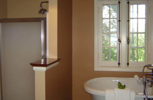 Shower and freestanding white bathtub in an elegant bathroom with a white window.