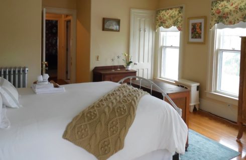 Beige bedroom with floral accents with white iron bed with white bedding and wooden cabinets.