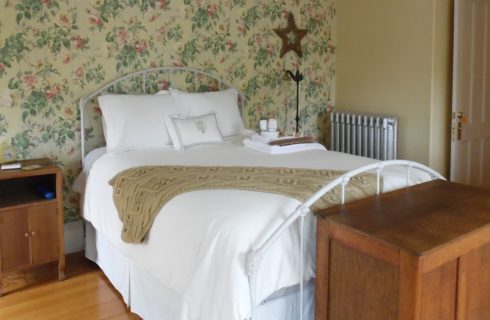 Guestroom with floral wallpaper holds an iron bed with white bedding.