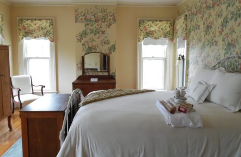 Bedroom with floral wallpaper accents with white iron bed with white bedding and wooden cabinets.