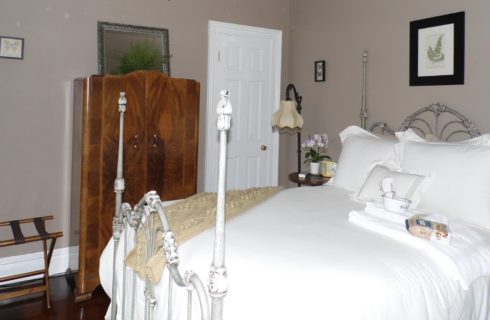 Room with beige walls, antique wooden wardrobe, and white iron bed made up in fluffy white bedding.