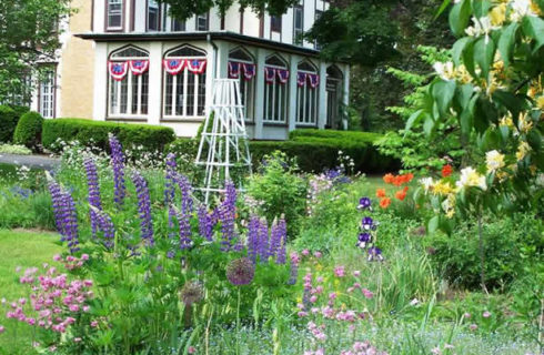 Tudor home fronted by a lush garden full of flowering plants and trees.