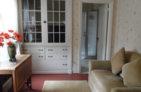 Peacceful guestroom with pale patterend wallpaper, a beige sofa and white built in cabinets.