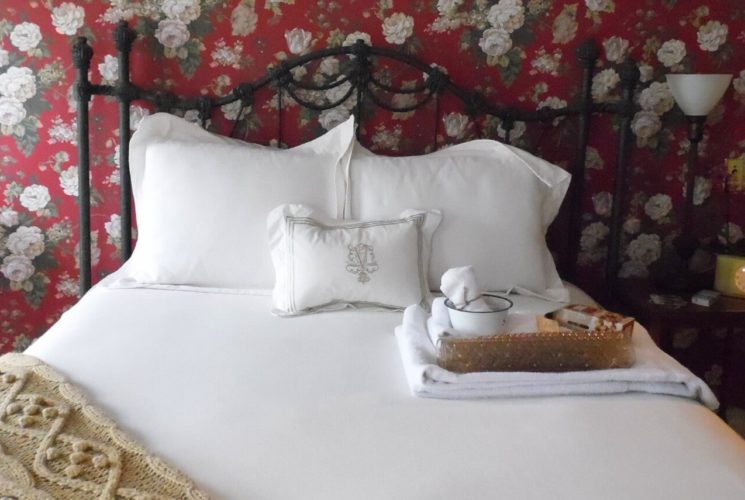 Bedroom with red floral wallpaper, white trim and a black iron bed made up with white bedding next to a white radiator.