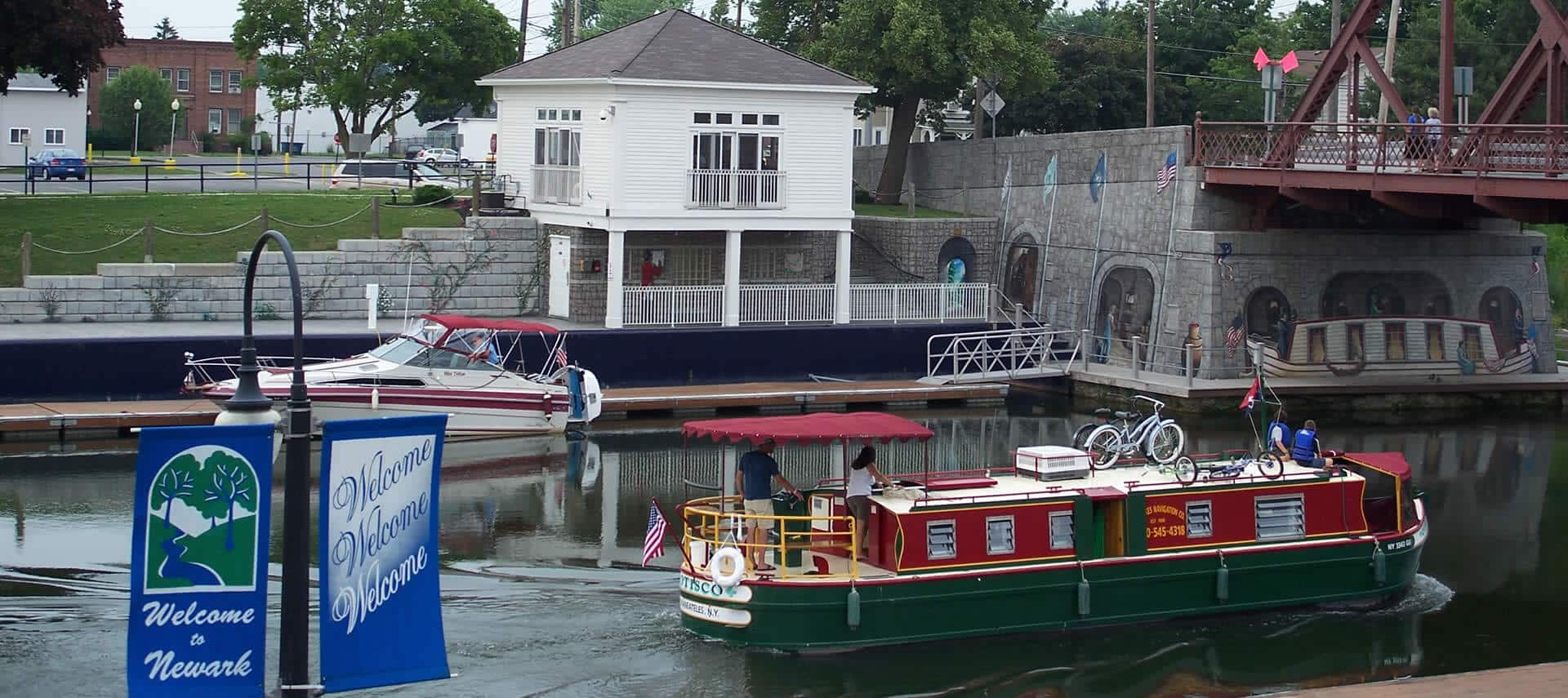 A large houseboat floats by a harbor wall with a small white building on top.