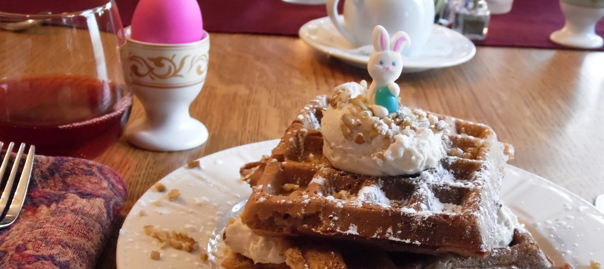 A stack of four waffles on a white plate topped with powdered sugar, whipped cream and chopped nuts.