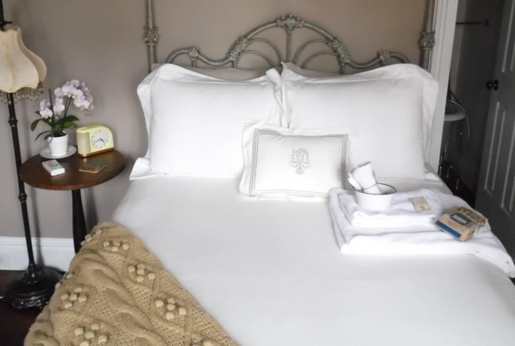 Ornate iron bed made up in fluffy white bedding with a wooden side table.