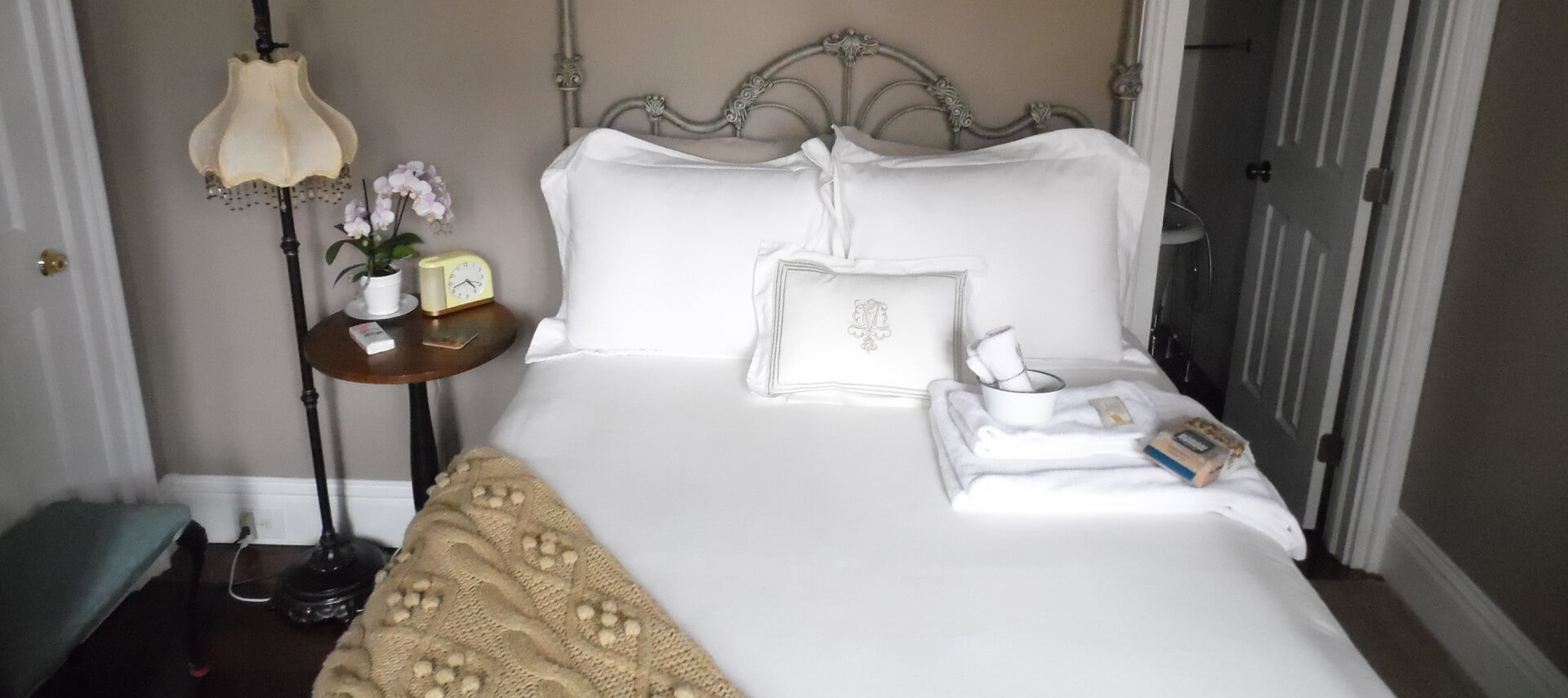 Ornate iron bed made up in fluffy white bedding with a wooden side table.