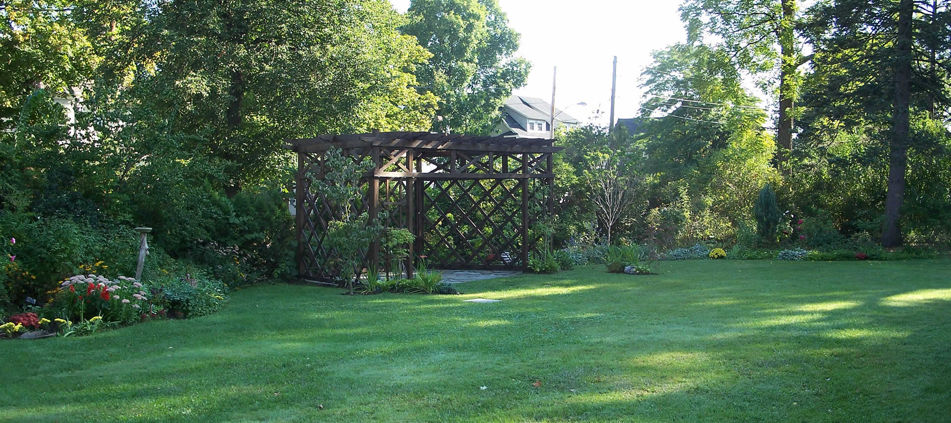 Deep green lawn with a wooden gazebo surrounded by large trees.