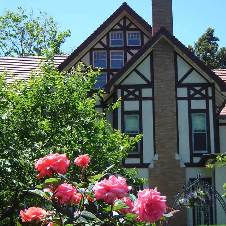 Tudor house with brick fireplace fronted by a pink rosebush.