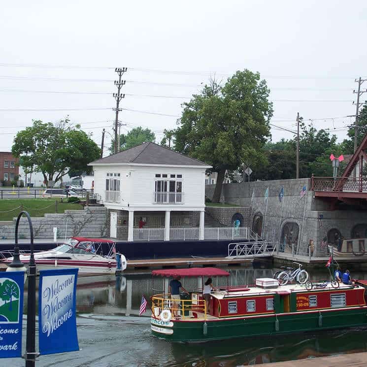 A large houseboat floats by a harbor wall with a small white building on top.