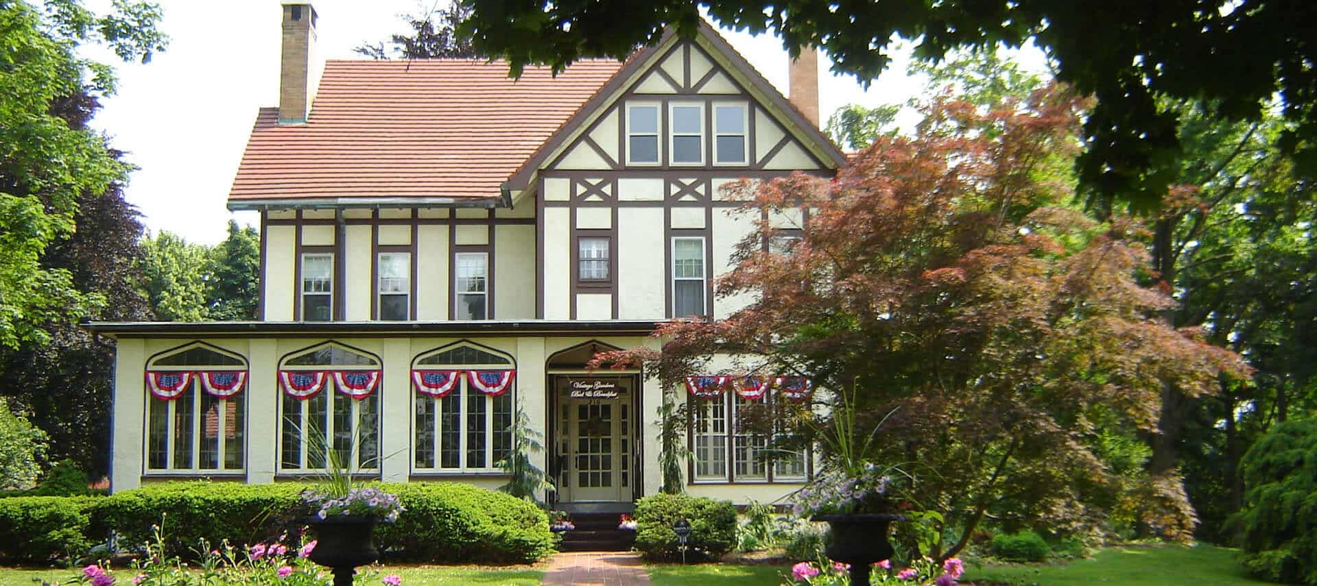 Historic two-story Tudor home on a green lawn surrounded by green trees.