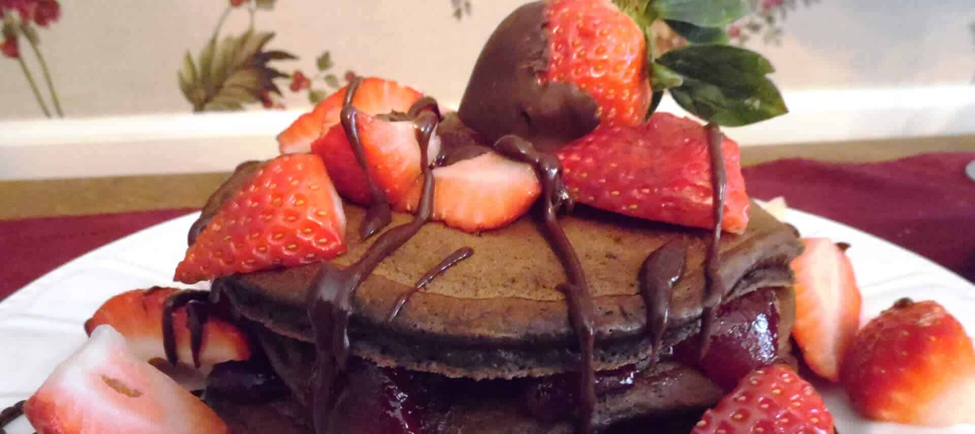 Chocolate pancakes topped with fresh strawberries and chocolate syrup. 