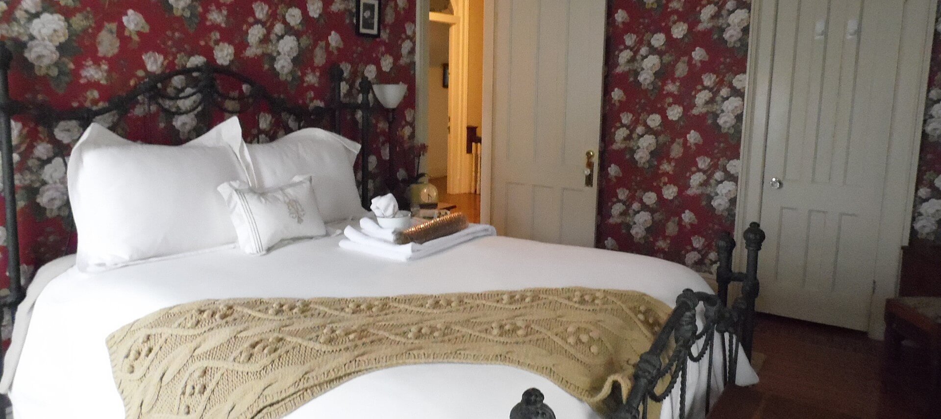 Queen wrought iron bed with white linens and floral wallpaper