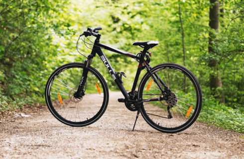 A black cruiser bike sits on a path through the woods.